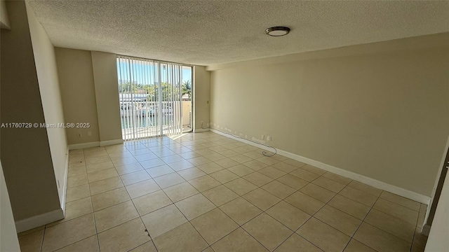 empty room featuring floor to ceiling windows, light tile patterned floors, baseboards, and a textured ceiling