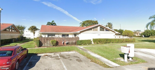 view of front of property with uncovered parking, a front lawn, and fence