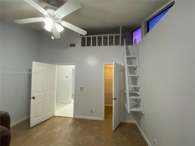 unfurnished bedroom featuring visible vents, baseboards, ceiling fan, and a towering ceiling