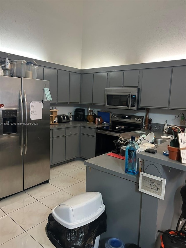 kitchen with light tile patterned flooring, gray cabinetry, stainless steel appliances, and a towering ceiling