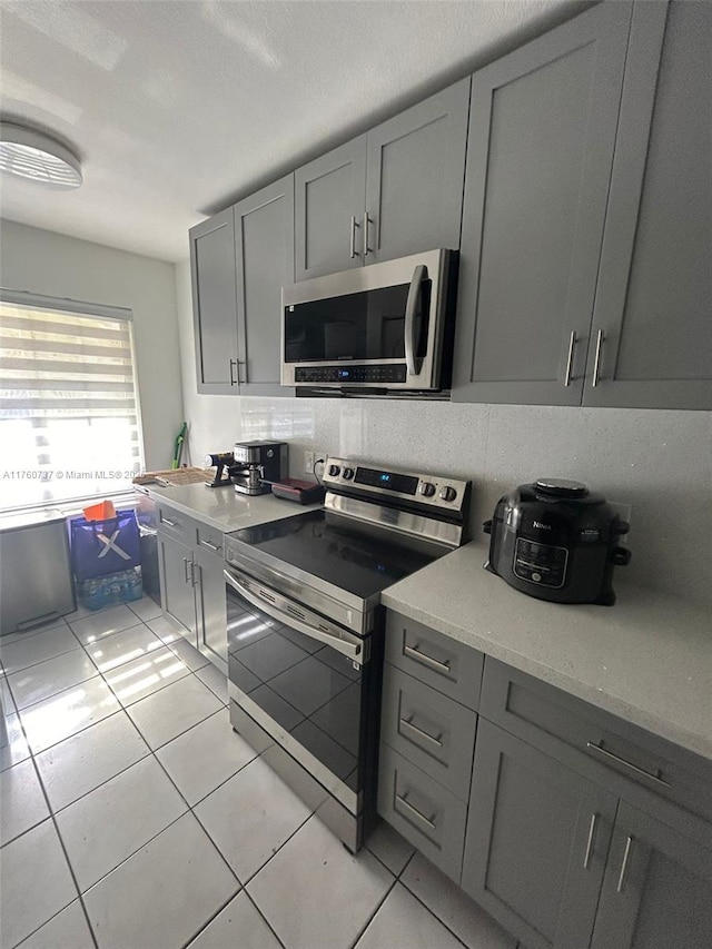 kitchen with light stone countertops, appliances with stainless steel finishes, light tile patterned flooring, and gray cabinets