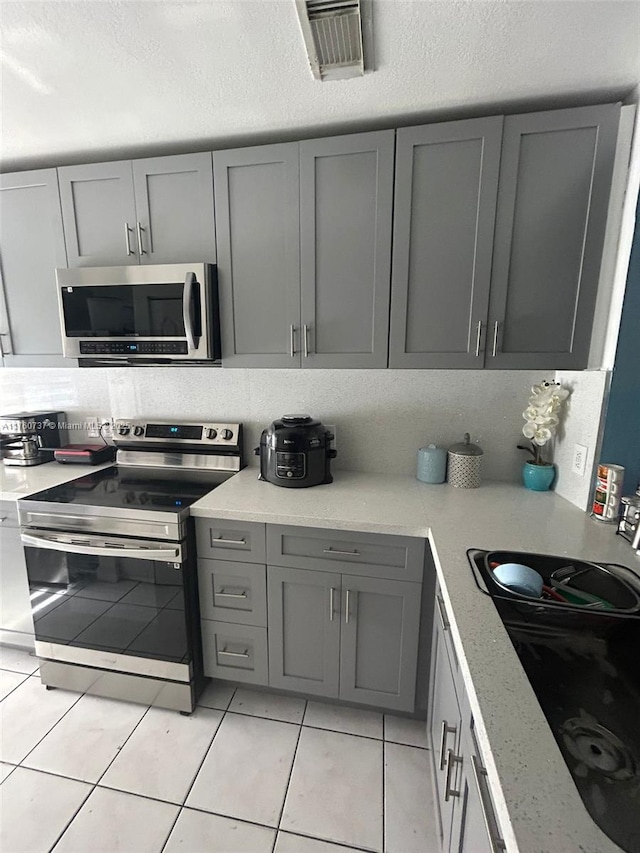 kitchen featuring visible vents, light tile patterned floors, decorative backsplash, gray cabinets, and stainless steel appliances