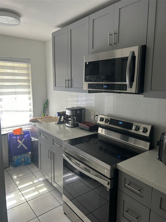 kitchen with light tile patterned floors, stainless steel appliances, light stone counters, and gray cabinetry