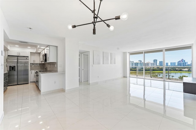 unfurnished living room featuring visible vents, a city view, light tile patterned flooring, a wall of windows, and baseboards