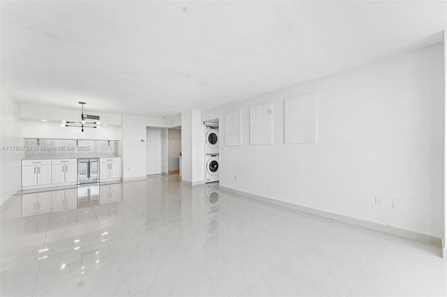 unfurnished living room with a notable chandelier, stacked washer and clothes dryer, and baseboards