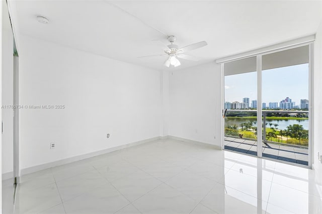 unfurnished room featuring baseboards, ceiling fan, floor to ceiling windows, a water view, and a view of city