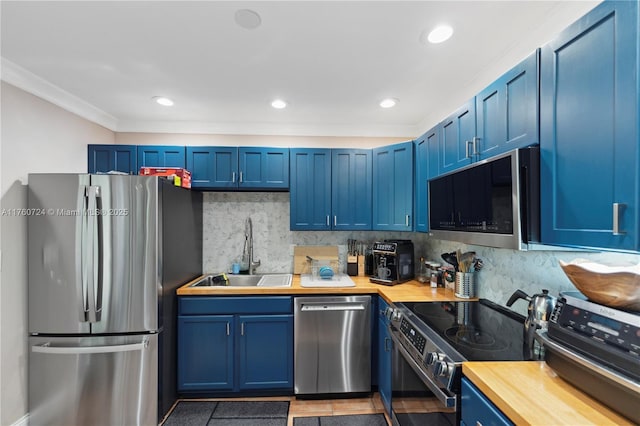 kitchen with blue cabinetry, butcher block countertops, decorative backsplash, appliances with stainless steel finishes, and a sink