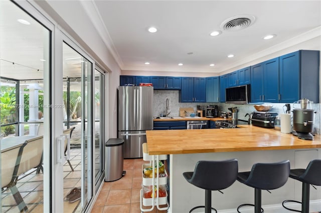 kitchen with visible vents, blue cabinetry, butcher block countertops, appliances with stainless steel finishes, and a peninsula