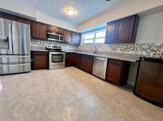 kitchen with dark brown cabinetry, decorative backsplash, appliances with stainless steel finishes, a textured ceiling, and a sink