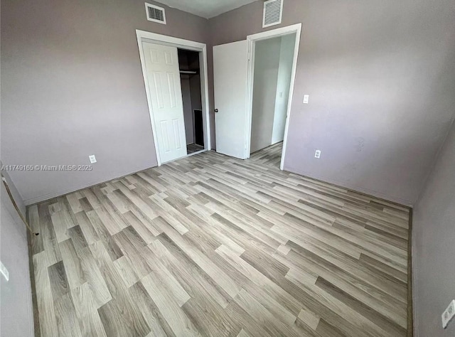 unfurnished bedroom featuring light wood-type flooring, visible vents, and a closet