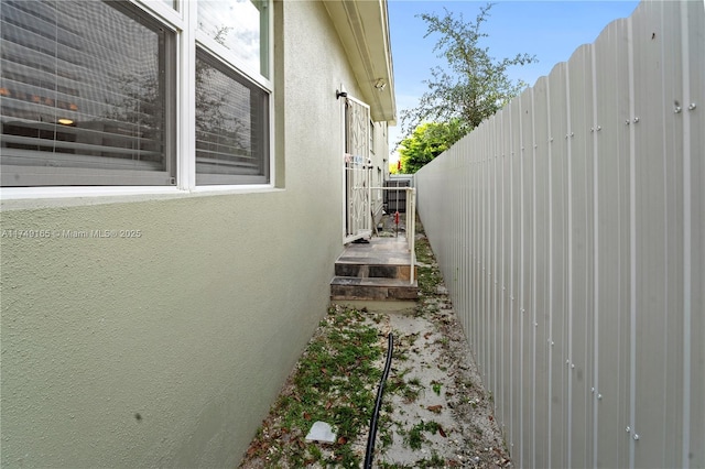 view of side of home with stucco siding and fence