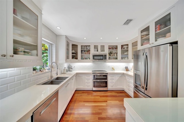 kitchen with visible vents, glass insert cabinets, decorative backsplash, appliances with stainless steel finishes, and a sink