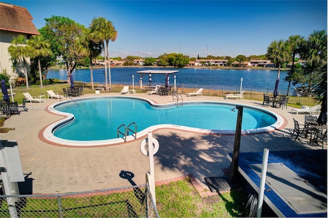 pool featuring a patio area, a water view, and fence