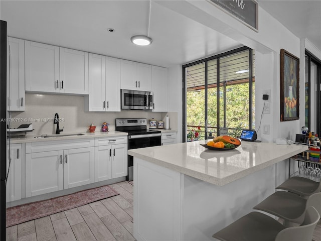 kitchen with light wood-style flooring, a sink, white cabinetry, stainless steel appliances, and a peninsula