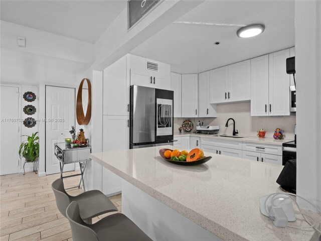 kitchen featuring light stone counters, light wood-style flooring, smart refrigerator, white cabinetry, and a sink