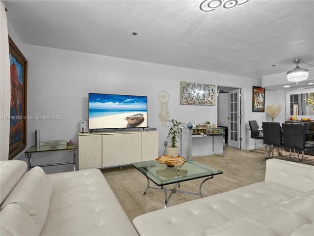 living room with a textured ceiling, light wood-type flooring, and baseboards