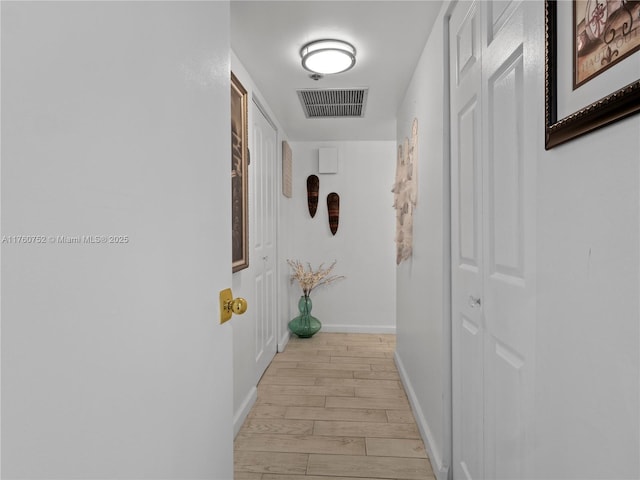 hall featuring light wood-style floors, visible vents, and baseboards