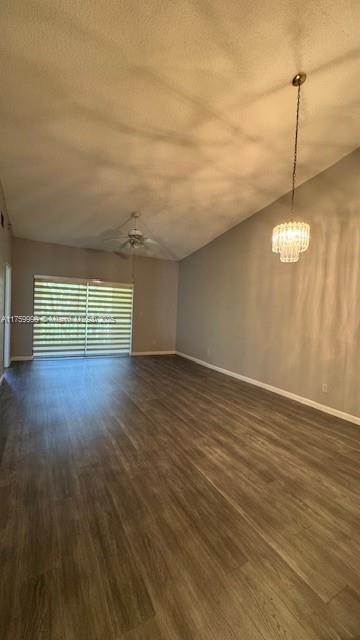 unfurnished room featuring baseboards, dark wood finished floors, vaulted ceiling, ceiling fan with notable chandelier, and a textured ceiling