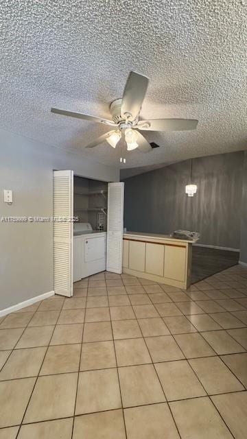 kitchen featuring light tile patterned floors, a ceiling fan, baseboards, a textured ceiling, and washer and clothes dryer