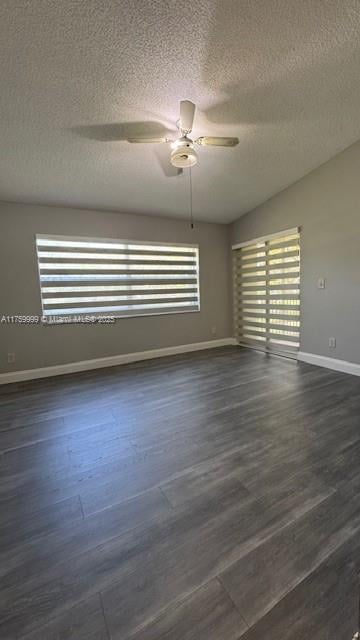 spare room with a textured ceiling, dark wood-type flooring, baseboards, and ceiling fan