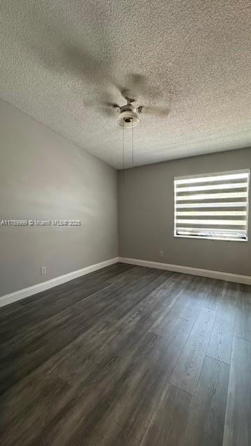 empty room featuring baseboards, a ceiling fan, dark wood-style flooring, and a textured ceiling