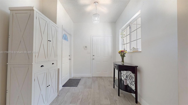 doorway featuring baseboards, light wood finished floors, and a textured ceiling