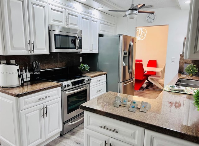 kitchen with a sink, backsplash, white cabinetry, stainless steel appliances, and ceiling fan