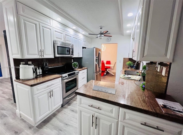 kitchen with a sink, backsplash, stainless steel appliances, light wood-style floors, and white cabinets