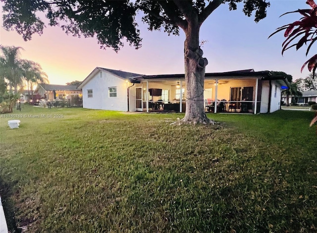 back of property at dusk featuring a patio and a lawn