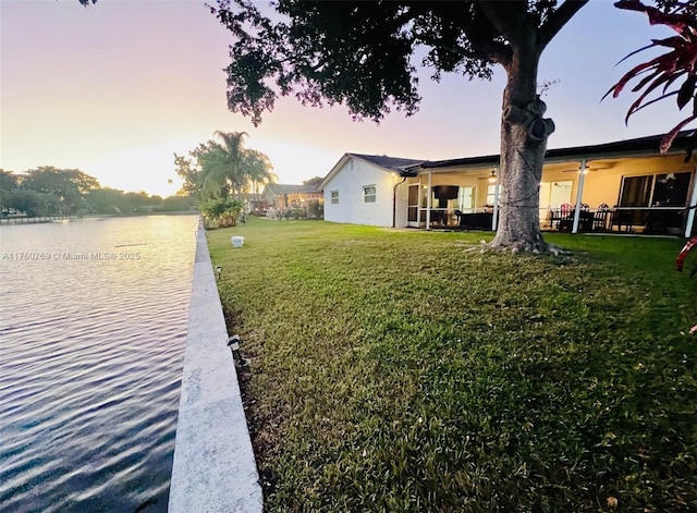 yard at dusk with a water view and ceiling fan