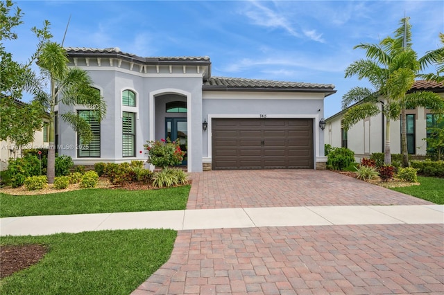 mediterranean / spanish house featuring a tiled roof, decorative driveway, a garage, and stucco siding