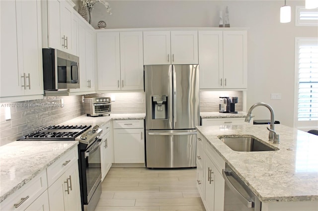 kitchen with a sink, backsplash, appliances with stainless steel finishes, white cabinetry, and a kitchen island with sink