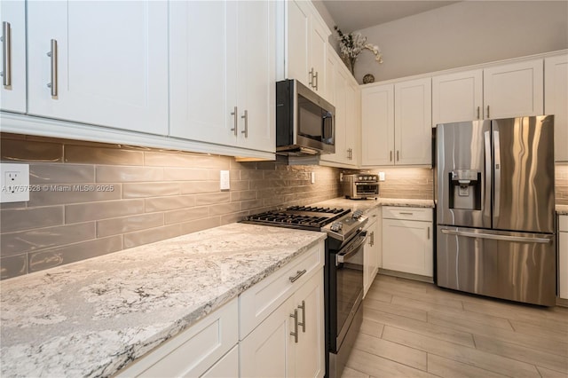 kitchen featuring backsplash, light stone counters, light wood-style floors, white cabinets, and stainless steel appliances