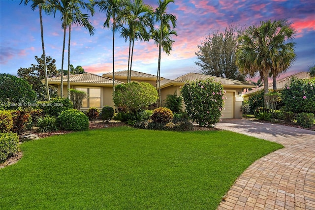 view of front of home with stucco siding, decorative driveway, a yard, an attached garage, and a tiled roof