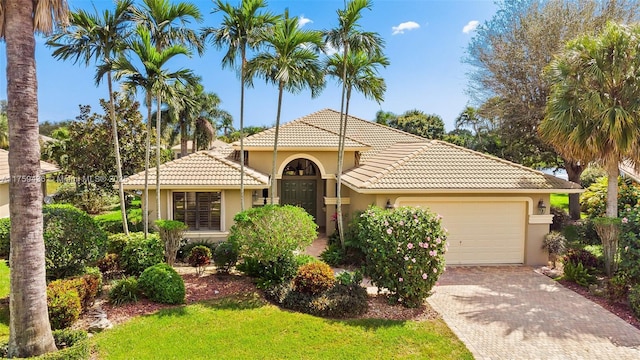 mediterranean / spanish-style home with stucco siding, a tiled roof, decorative driveway, and a garage