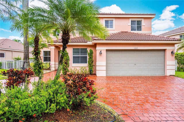 mediterranean / spanish-style house with stucco siding, decorative driveway, fence, a garage, and a tiled roof