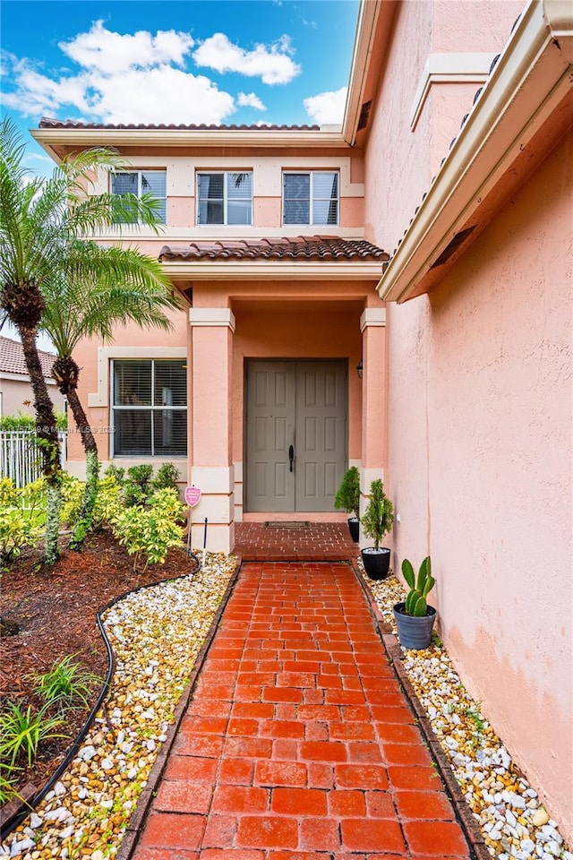 entrance to property with stucco siding, fence, and a tile roof