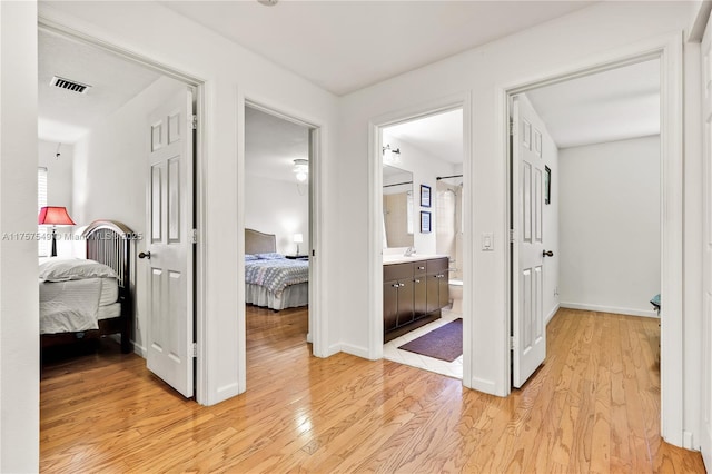 hallway featuring a sink, visible vents, baseboards, and light wood finished floors