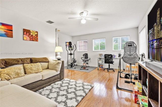 living area featuring baseboards, visible vents, light wood finished floors, ceiling fan, and a textured ceiling