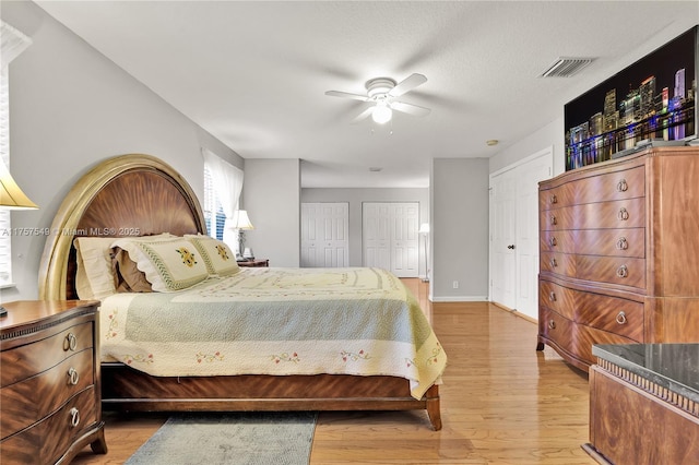 bedroom featuring baseboards, visible vents, ceiling fan, multiple closets, and light wood-type flooring