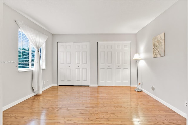 unfurnished bedroom featuring light wood finished floors, baseboards, and multiple closets