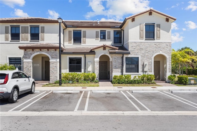 view of front of home featuring a tiled roof, uncovered parking, stone siding, and stucco siding