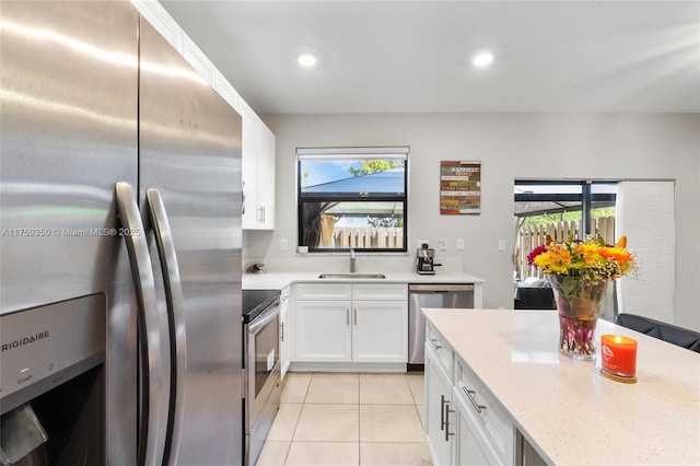 kitchen featuring white cabinetry, light stone counters, a sink, appliances with stainless steel finishes, and light tile patterned floors