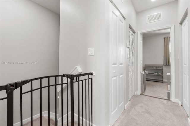 hallway with carpet floors, baseboards, visible vents, and an upstairs landing