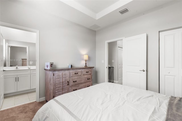 carpeted bedroom with visible vents, tile patterned flooring, a closet, ensuite bathroom, and a sink