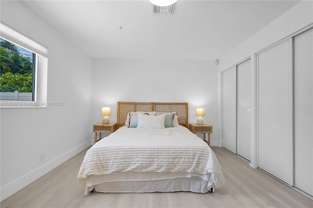 bedroom featuring visible vents, baseboards, multiple closets, and light wood finished floors