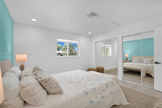 bedroom featuring visible vents, two closets, attic access, recessed lighting, and wood finished floors