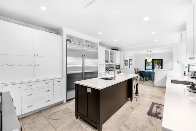 kitchen featuring a sink, stainless steel built in refrigerator, white cabinets, and a center island with sink