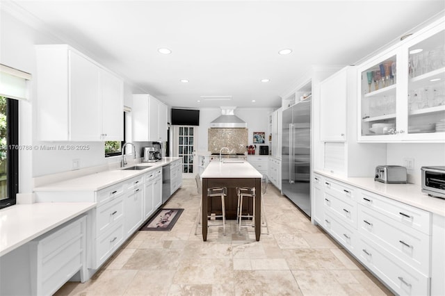 kitchen with white cabinetry, wall chimney range hood, appliances with stainless steel finishes, and a sink