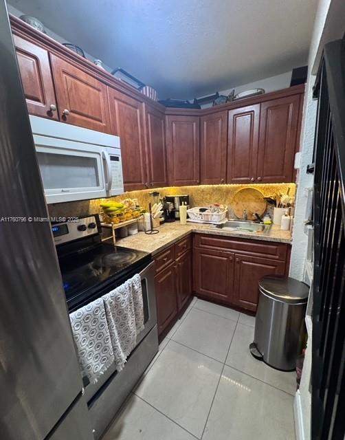 kitchen with stainless steel electric range oven, white microwave, a sink, light countertops, and backsplash